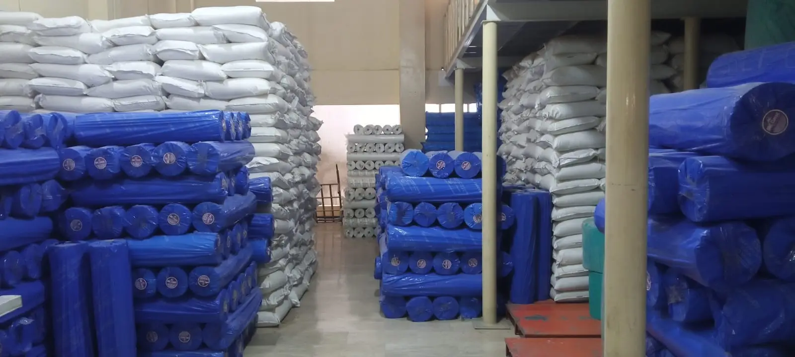 Warehouse aisle lined with blue fabric rolls and white bagged stock